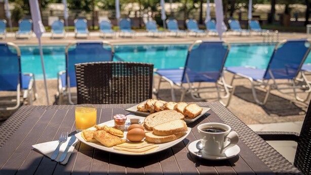 A breakfast table with toast, eggs, and juice, overlooking a pool with lounge chairs. - Apollo Hotel (Zakynthos)