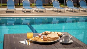 A poolside breakfast setup with a plate of toast, eggs, and juice, and a cup of coffee on a table. - Apollo Hotel (Zakynthos)