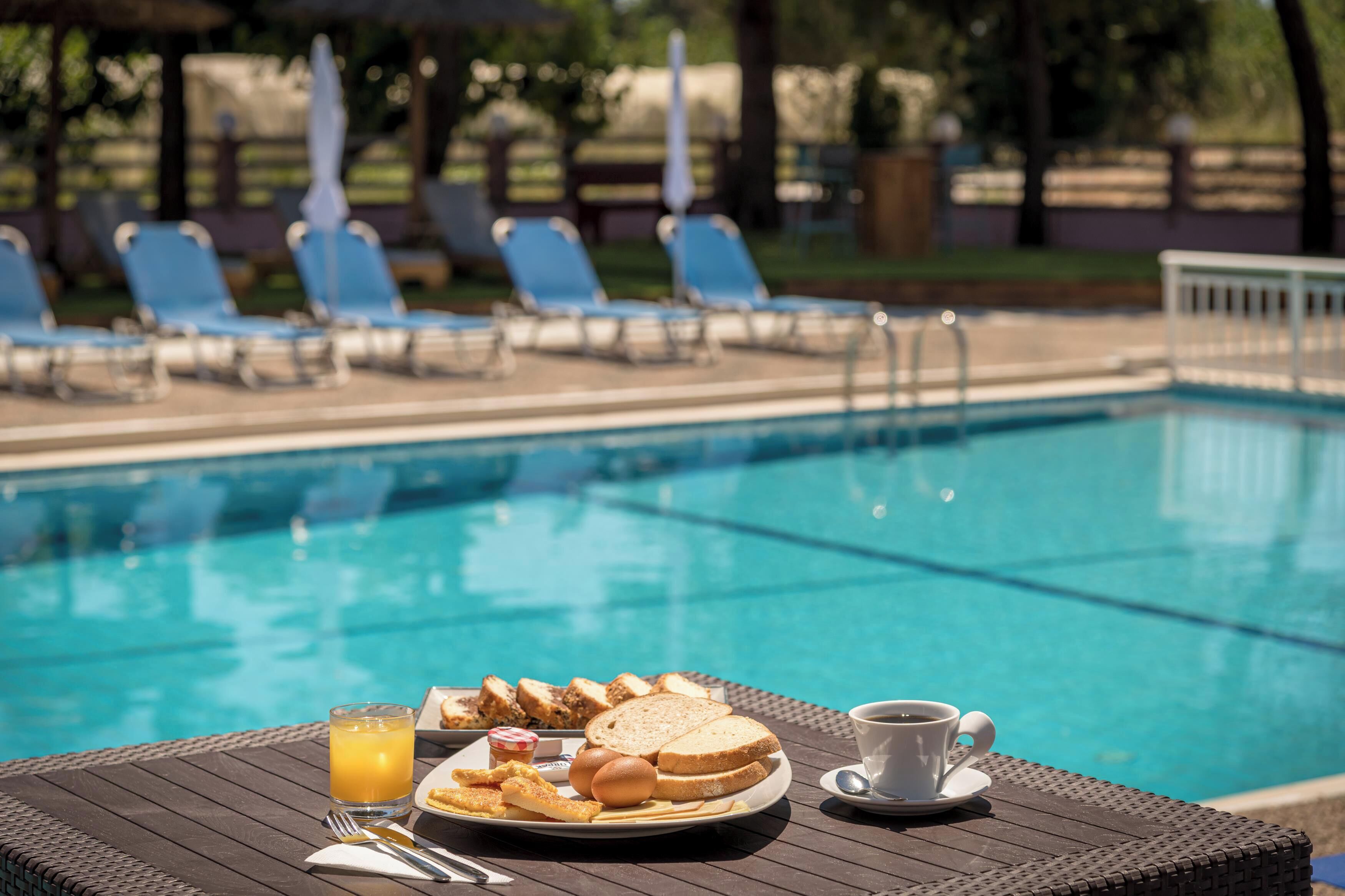 A poolside breakfast setup with a plate of food, a glass of orange juice, and a cup of coffee.