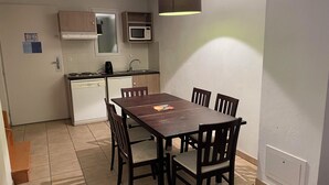 A compact kitchen with a dining table, chairs, a microwave, and a hanging light fixture. - Apt 5/6 pers.in the countryside, swimming pool, golf, horse riding (Barbaste)