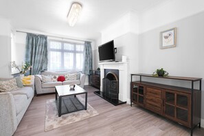 A living room with a sofa, coffee table, fireplace, TV, and a cabinet. - Spacious 5 Bedroom Family Home in Harrow (Harrow)