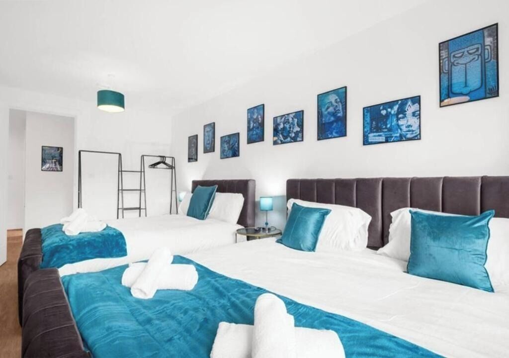 A hotel room with two beds, a wardrobe, a desk, and a wall with framed artwork.