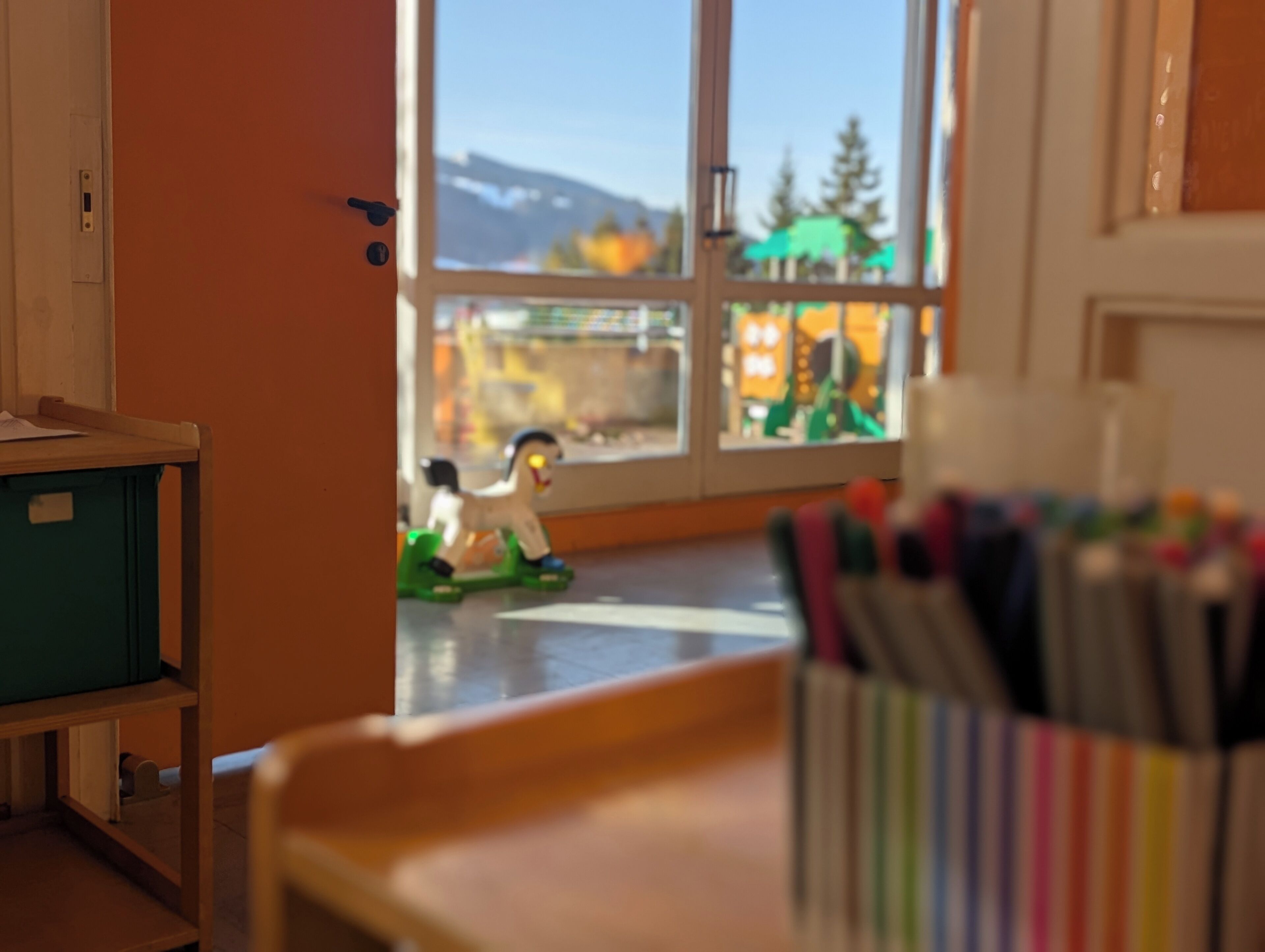 Una habitación con ventana, un juguete en el suelo y un escritorio con bolígrafos.