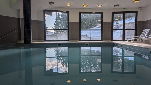 An indoor swimming pool with clear glass walls, a tiled floor, and ceiling lights. - Villages vacances Cévéo de Bois d'Amont (Bois-d'Amont)