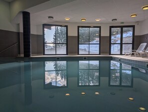En inomhuspool med väggar av genomskinligt glas, ett kaklat golv och takbelysning.