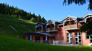 A multi-story building with balconies, a fenced area, and a grassy slope. - Villages vacances Cévéo de Bois d'Amont (Bois-d'Amont)