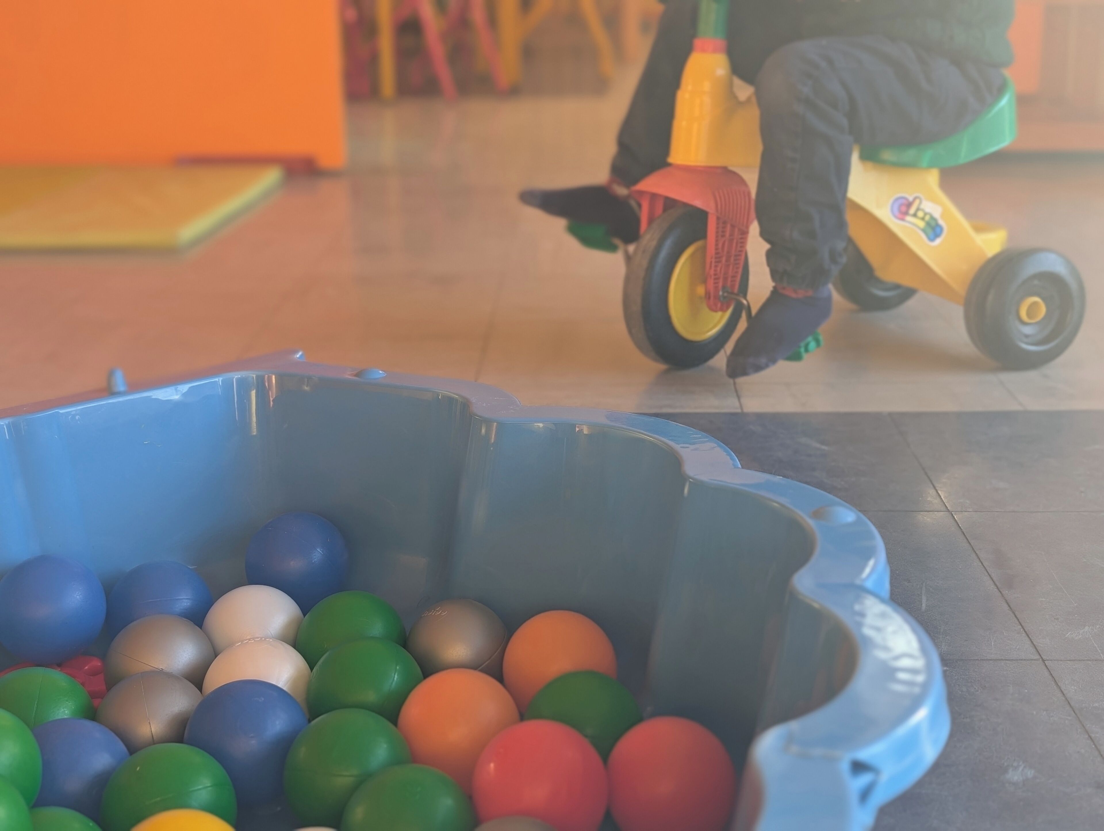 A child riding a toy tricycle indoors.