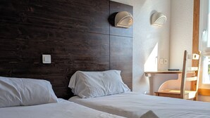 A hotel room with two beds, a wooden headboard, a desk with a chair, and a window. - Villages vacances Cévéo de Bois d'Amont (Bois-d'Amont)