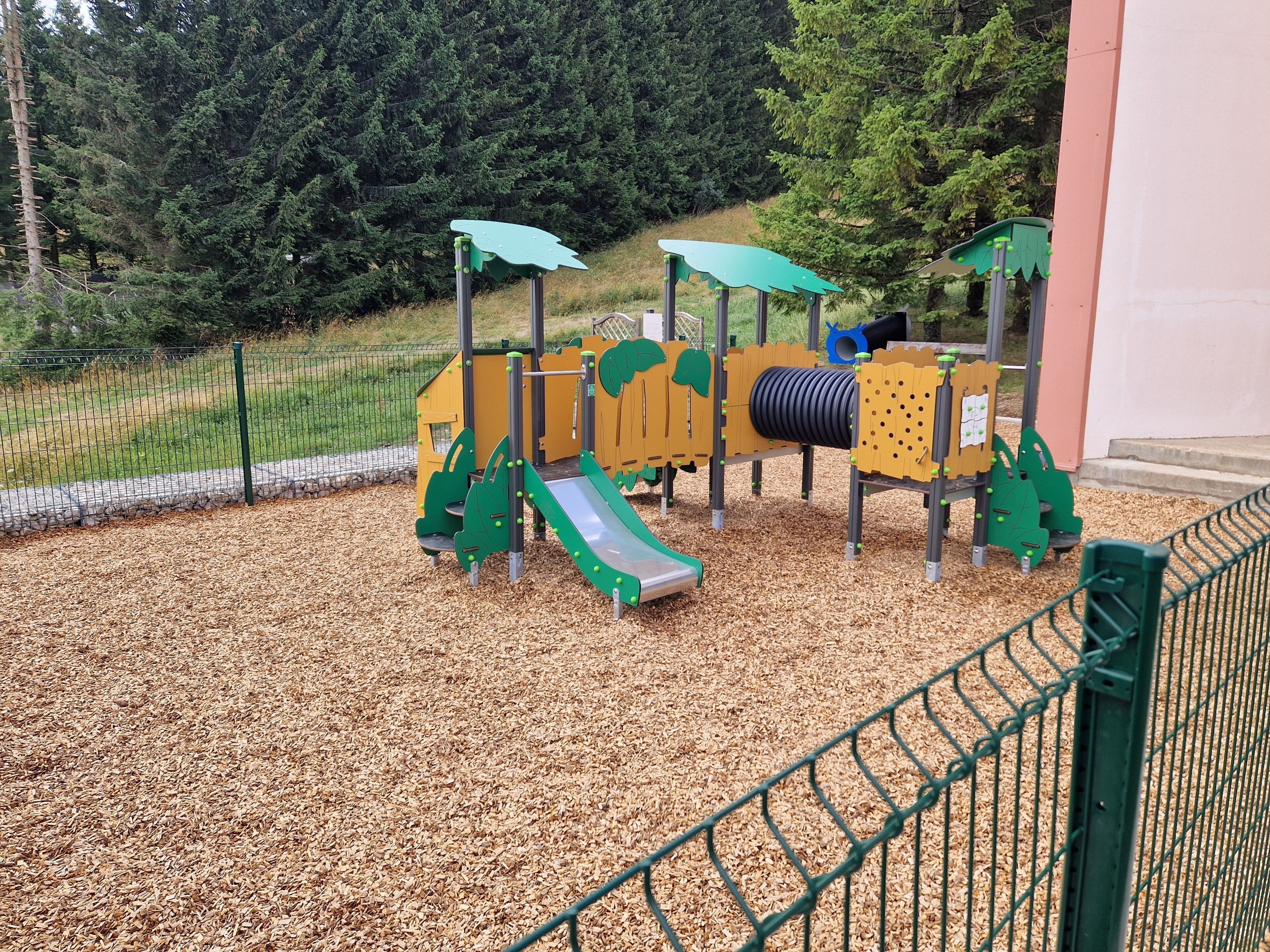 A playground with a slide, climbing structures, and a netted safety fence.