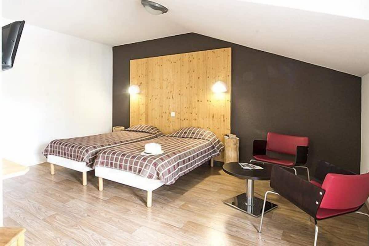 Ein Schlafzimmer mit zwei Betten, einem kleinen Tisch, einem Stuhl und einer Wand mit Holzpaneelen.
