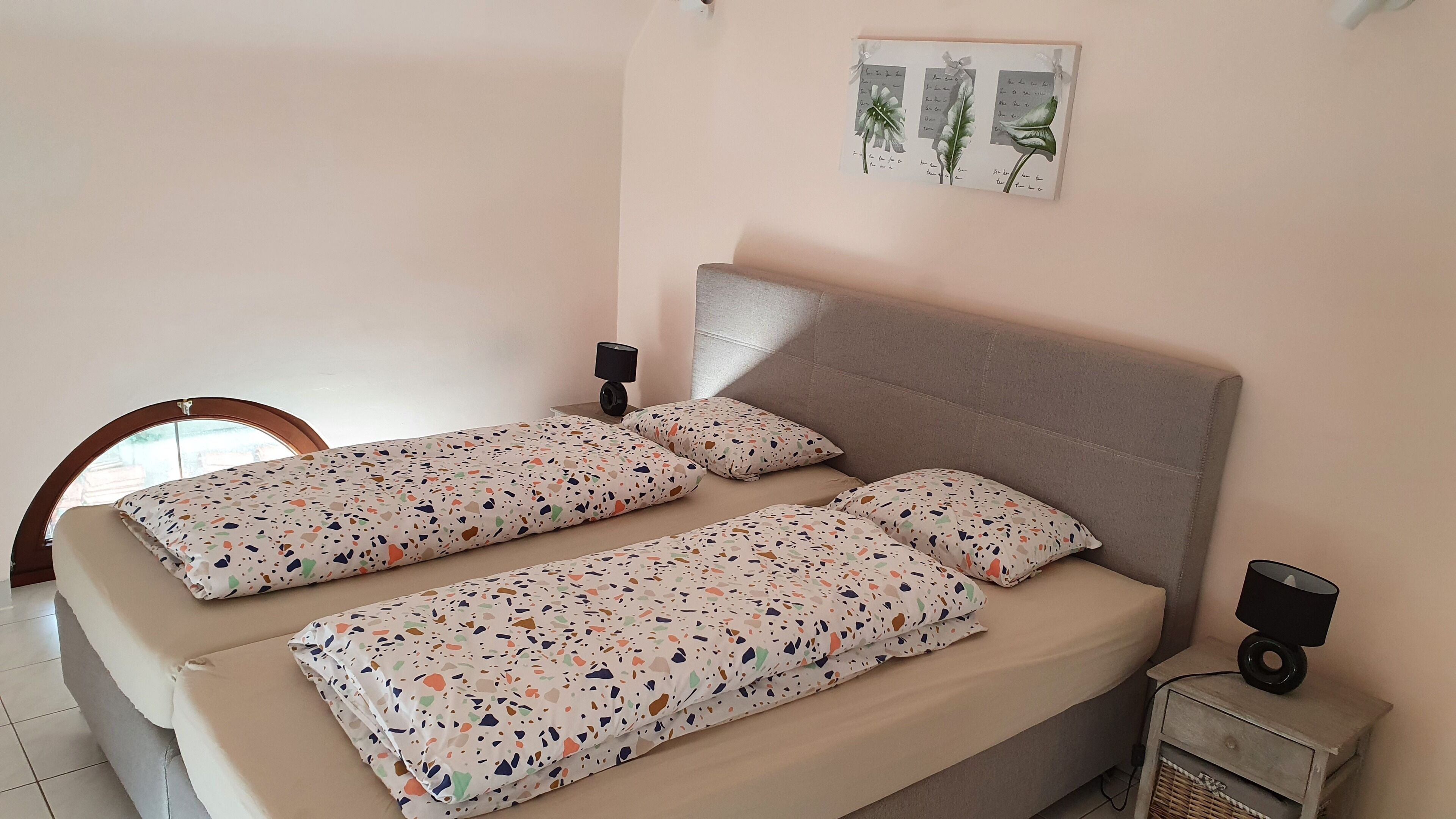A double bed with patterned bedding, a bedside lamp, and a small table with a lamp.