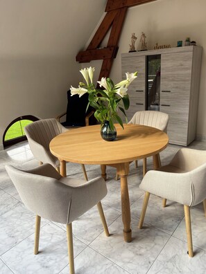 Ein runder Holztisch mit Blumen in einer Vase, umgeben von vier gepolsterten Stühlen mit Holzbeinen, auf einem gefliesten Boden.