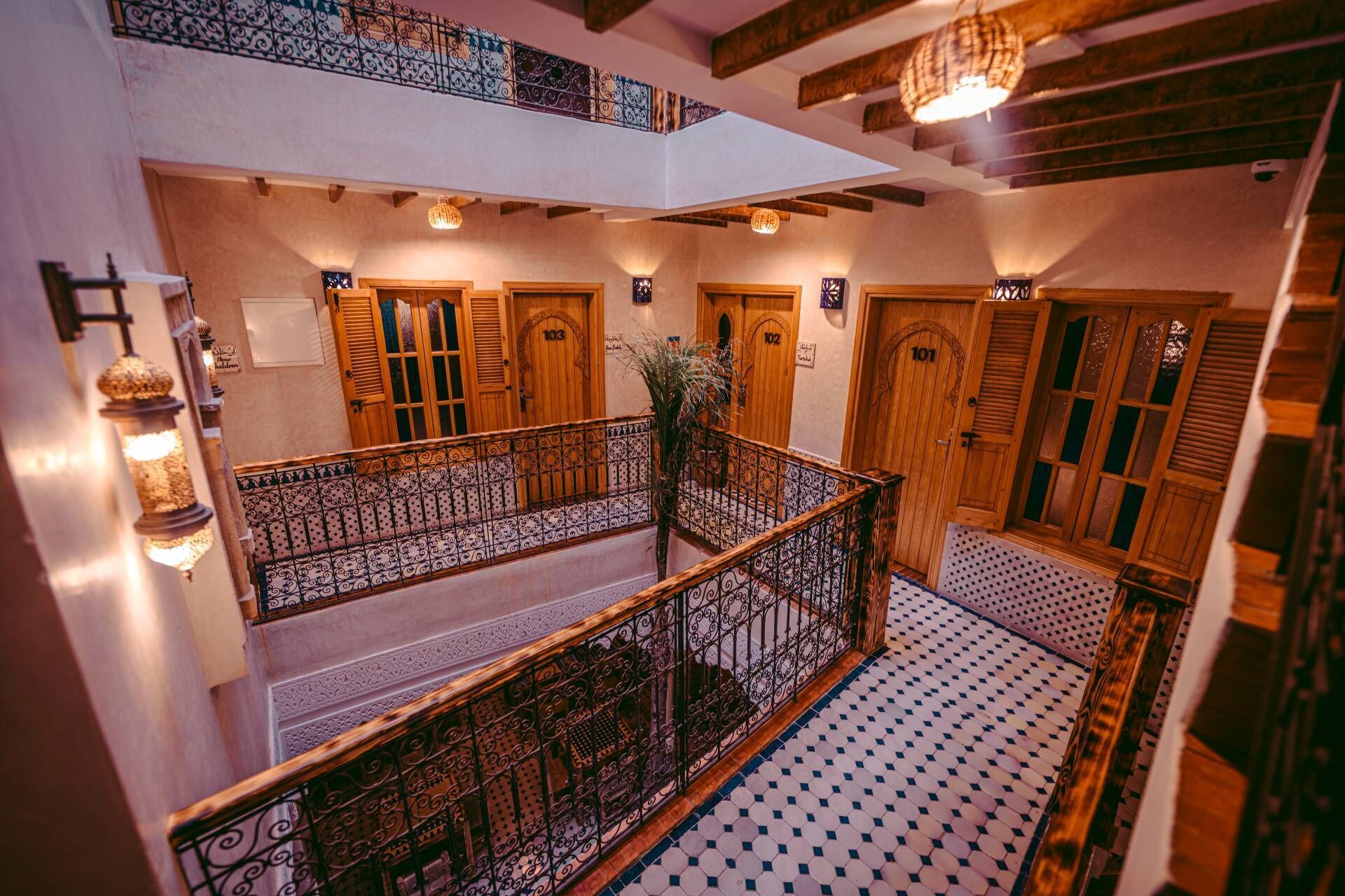 Interior de un hotel de varios niveles con puertas de madera, barandillas de hierro forjado y piso con diseños.