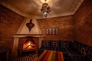 Una habitación acogedora con chimenea de ladrillo, un sofá estampado y una lámpara colgante.