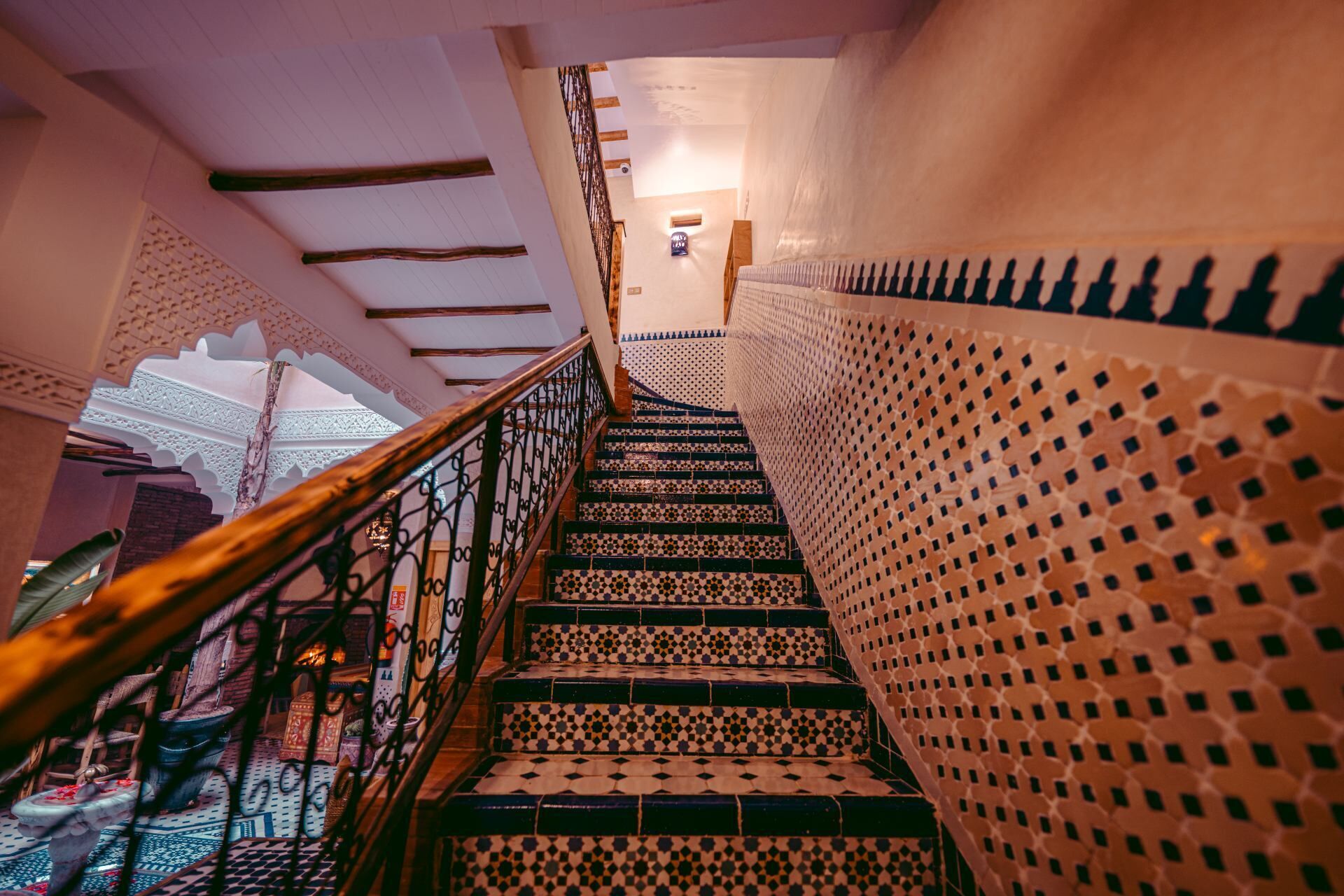 Una escalera con barandillas ornamentales y baldosas estampadas, que conduce a una habitación con un techo decorativo.