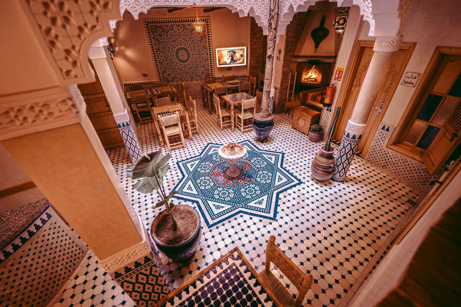 A traditional Moroccan interior with a central fountain, patterned tiles, and a fireplace.