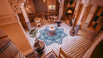 A traditional Moroccan interior with a central fountain, patterned tiles, and a fireplace.