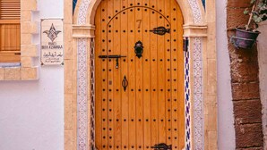 A traditional wooden door with a metal handle, flanked by decorative steps and a tiled wall. - Riad Bleu Azahraa (Safi)