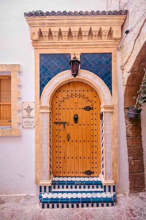 Una puerta de madera tradicional con manija metálica, flanqueada por escalones decorativos y un muro de azulejos.