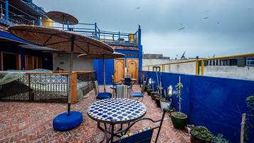 Une terrasse sur le toit, avec une table ronde, des chaises et des plantes en pot.