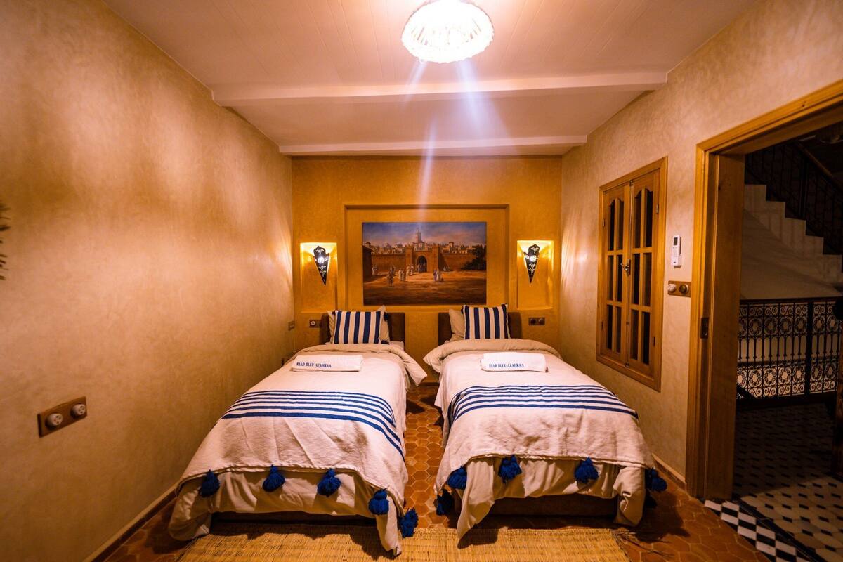 A hotel room with two beds, a painting on the wall, and a staircase.
