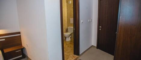 Un pasillo estrecho con un banco de madera, una puerta que da a un baño y suelo alfombrado.