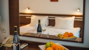 A hotel room with a bed, a bedside table with a phone, a bottle, a glass, and a tray with fruit. - Deva Hotel - All Inclusive (Sunny Beach)