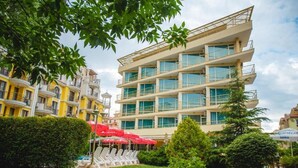 A multi-story hotel with balconies, a garden area with sun loungers, and a poolside area with umbrellas. - Deva Hotel - All Inclusive (Sunny Beach)