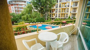 A balcony with a pool, white chairs, and a view of surrounding buildings. - Deva Hotel - All Inclusive (Sunny Beach)