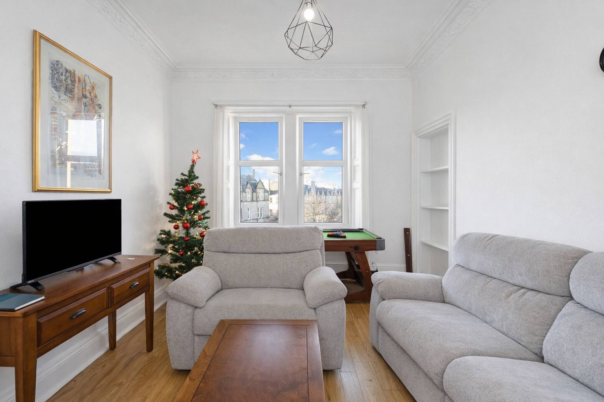 A living room with a sofa, a coffee table, a TV on a wooden stand, a Christmas tree, and a pool table.