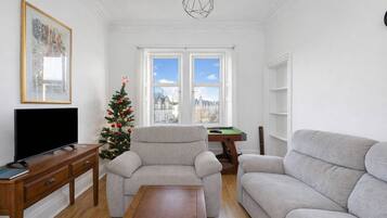 A living room with a sofa, a coffee table, a TV on a wooden stand, a Christmas tree, and a pool table.