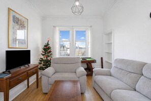 A living room with a sofa, a coffee table, a TV on a wooden stand, a Christmas tree, and a pool table. - Leith Walk 2BR | Pool Table & Bath Tub | Tram Stop (Edinburgh)