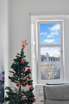 A Christmas tree with ornaments and a star topper in a room with a window. - Leith Walk 2BR | Pool Table & Bath Tub | Tram Stop (Edinburgh)