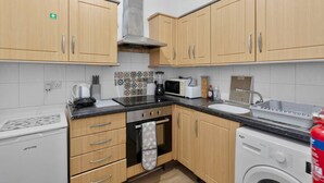 A compact kitchen with wooden cabinets, a microwave, a coffee maker, a washing machine, and a tiled backsplash. - Leith Walk 2BR | Pool Table & Bath Tub | Tram Stop (Edinburgh)