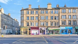 A street view with buildings, shops, and a pedestrian crossing. - Leith Walk 2BR | Pool Table & Bath Tub | Tram Stop (Edinburgh)