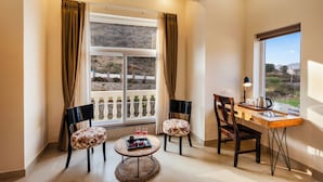 A room with a large window, two chairs, a small table with a tray of items, and a desk with a lamp and laptop. - ELIVAAS Mandovar Mountain Valley Retreat (Udaipur)