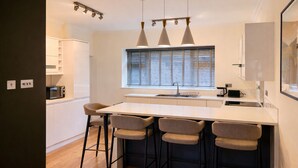 Une cuisine moderne dotée d’un îlot central, de tabourets de bar, de luminaires suspendus et d’une fenêtre avec des stores.