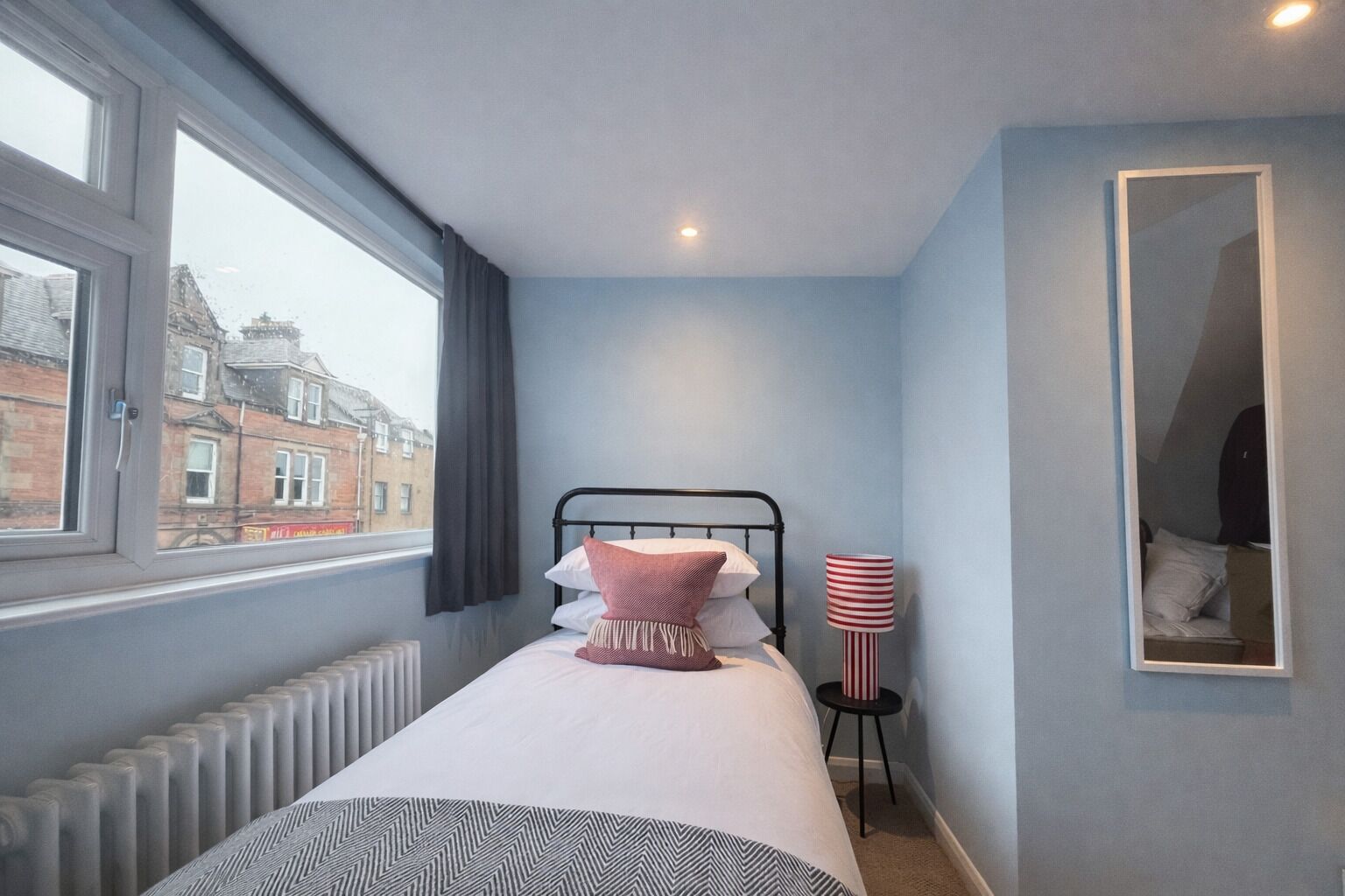 Une chambre à coucher avec un lit, une fenêtre, un radiateur, une lampe et un miroir.