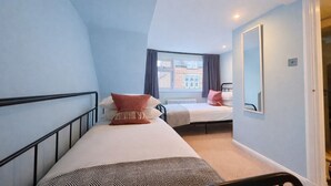 Une chambre avec deux lits simples, une fenêtre avec des rideaux, un radiateur et un miroir au mur.