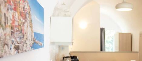 A room with a dining area, a white cabinet, a hanging light fixture, and a painting of a coastal town.