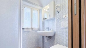 Un baño con inodoro blanco, lavabo, espejo y ventana.