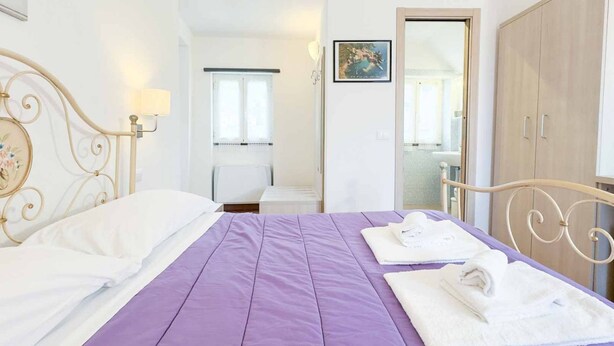 Un dormitorio con una cama, una mesita de noche, una lámpara, una ventana y un armario.
