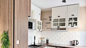A modern kitchen with white cabinetry, a wooden accent wall, a microwave, a sink, and a coffee maker. - Pearly EuroPoint (Saint-Louis)
