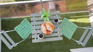 A rooftop terrace with a table set for two, surrounded by green cushioned seating. - Pearly EuroPoint (Saint-Louis)