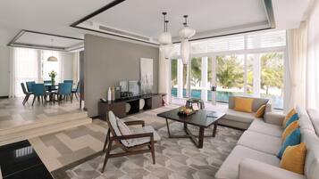 Una sala moderna con sofá, mesa de centro y sillas. Hay un comedor con mesa y sillas. La habitación tiene ventanas grandes con vista a palmeras y una piscina.