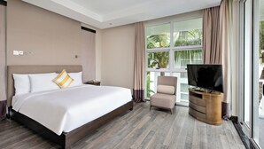 A hotel room with a large bed, a TV on a wooden stand, a chair, and a window with curtains. - Villa Premier Village Da Nang Abogo (Da Nang)