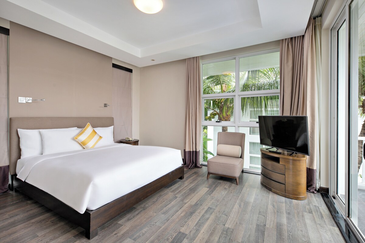 Una camera d'albergo con un letto grande, una televisione su un mobile in legno, una sedia e una finestra con tende.