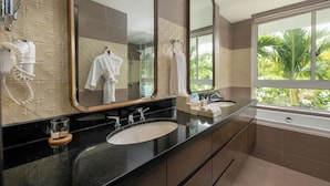 A bathroom with a large mirror, a sink, a shower, and a window with a view of greenery. - Villa Premier Village Da Nang Abogo (Da Nang)