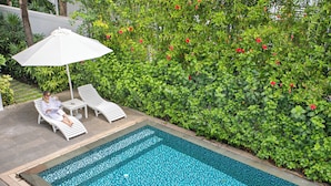 A swimming pool with white lounge chairs and an umbrella, surrounded by lush greenery and red flowers. - Villa Premier Village Da Nang Abogo (Da Nang)