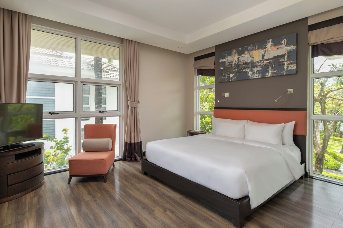 Una camera d'albergo con un letto grande, una televisione, una poltrona e un quadro appeso al muro.